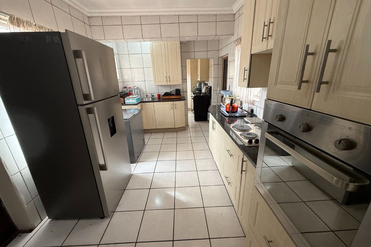 A functional kitchen featuring built-in cabinetry, granite countertops, an integrated oven, and an electric hob, with tiled flooring and wall finishes throughout.