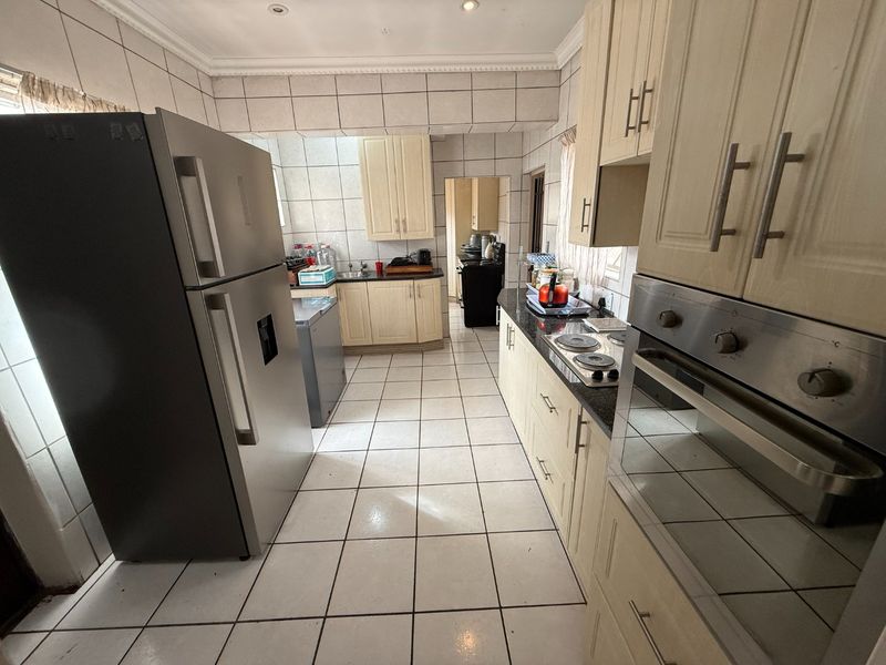 A functional kitchen featuring built-in cabinetry, granite countertops, an integrated oven, and an electric hob, with tiled flooring and wall finishes throughout.