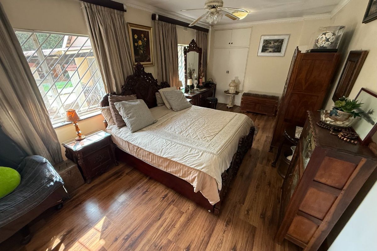 A spacious bedroom featuring laminate flooring, built-in cupboards, and a ceiling fan, with large windows fitted with security bars.