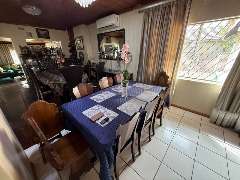 A dining room featuring tiled flooring, a timber-paneled ceiling, and a wall-mounted air conditioning unit, with natural light entering through a window with security bars.