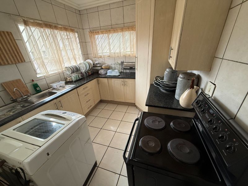 A functional kitchen featuring light-toned cabinetry, dark granite countertops, tiled walls, and a freestanding electric stove with ample natural light.