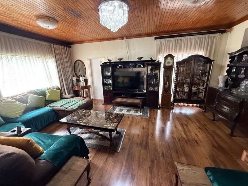 Spacious living room featuring warm timber ceilings, laminate flooring, and a decorative crystal chandelier, offering a comfortable and traditional atmosphere.