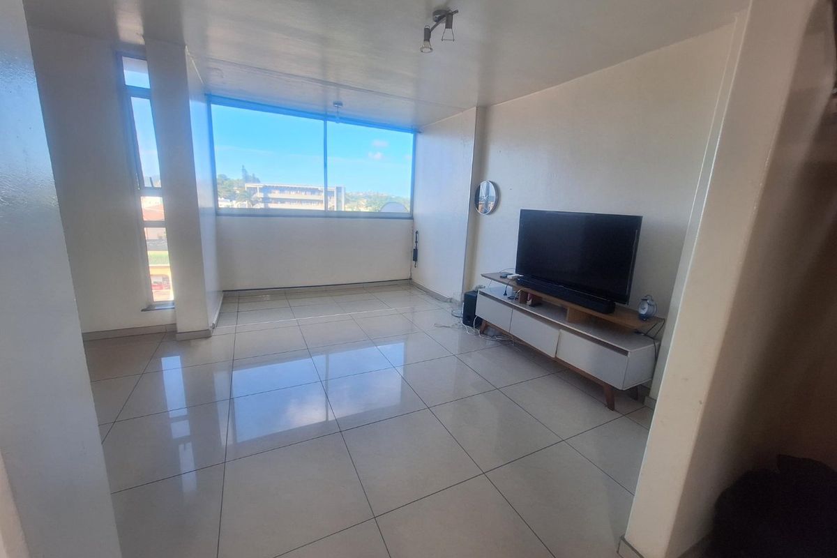 A bright living room featuring large windows with natural light and neutral tiled flooring throughout.