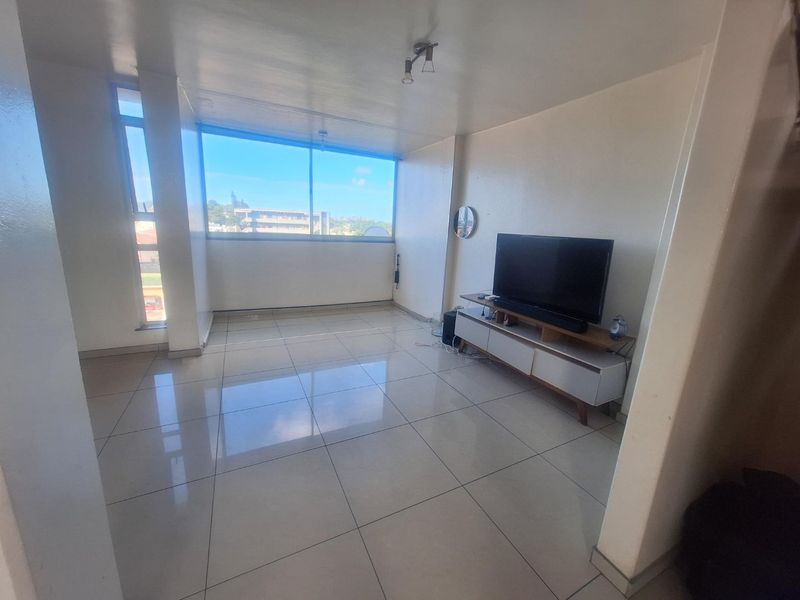 A bright living room featuring large windows with natural light and neutral tiled flooring throughout.
