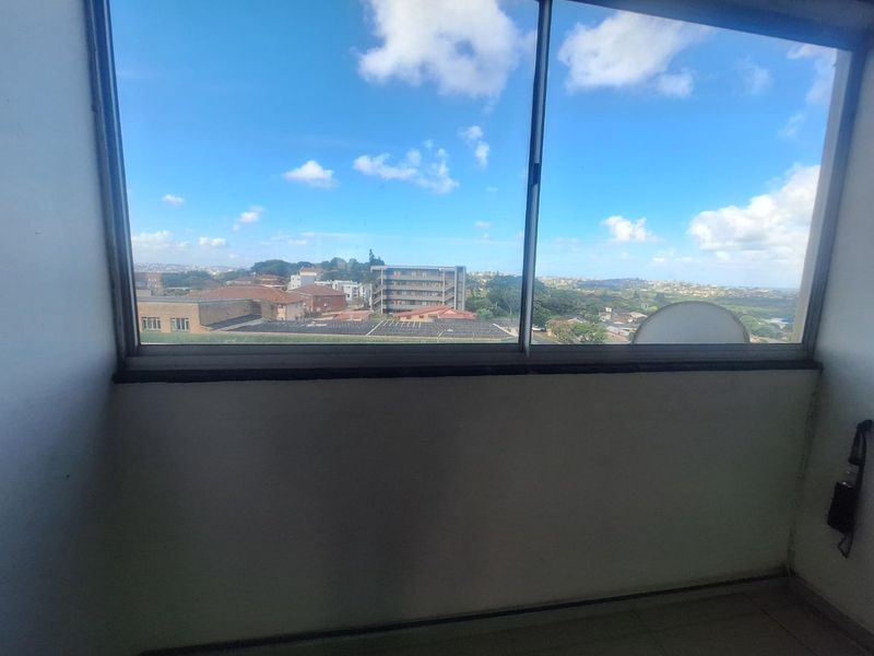 An interior view looking out through a large sliding window, showcasing an elevated perspective of the surrounding urban landscape and neighborhood.