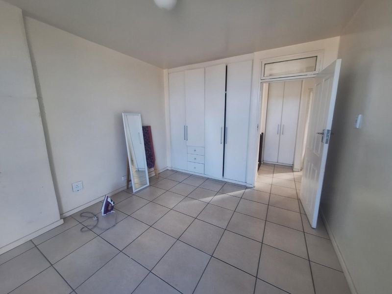 A spacious bedroom featuring neutral tiled flooring and extensive built-in cupboard storage, offering a clean and functional living space.
