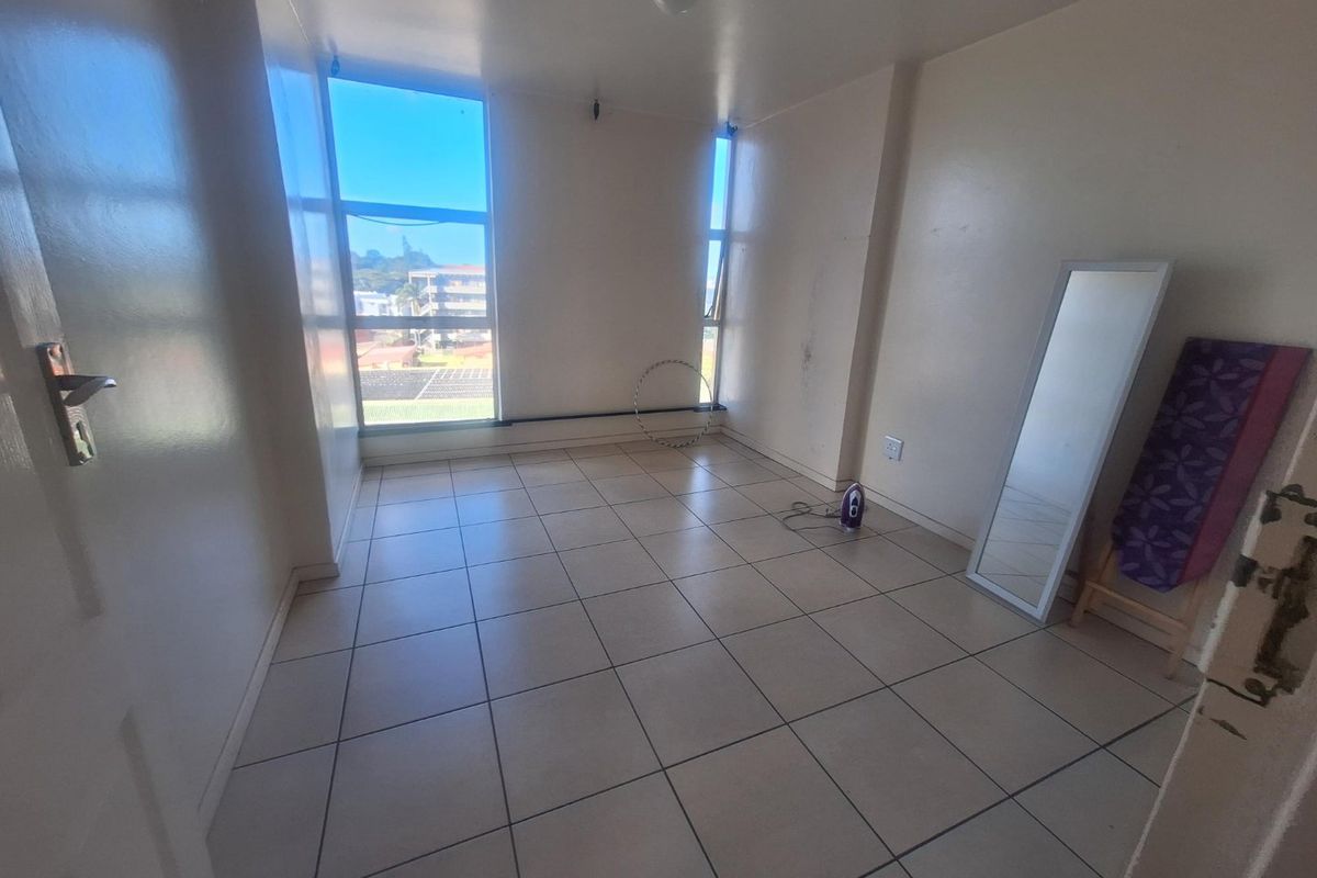 A vacant bedroom featuring neutral tiled flooring and large windows that provide natural light and an urban view.