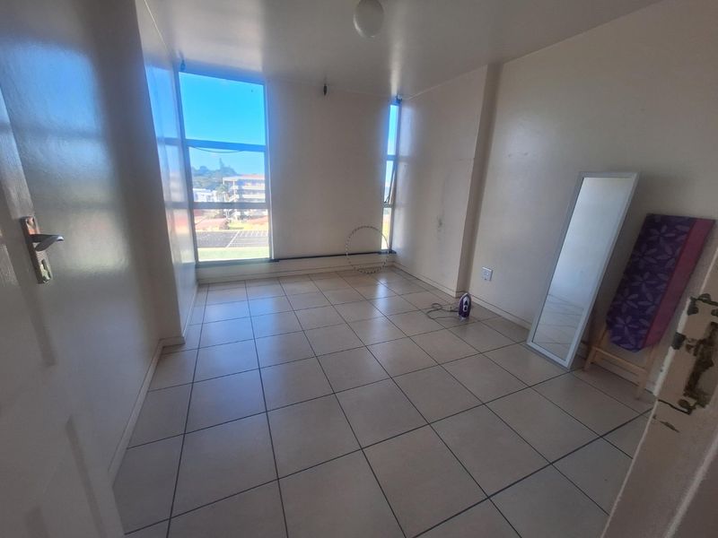 A vacant bedroom featuring neutral tiled flooring and large windows that provide natural light and an urban view.