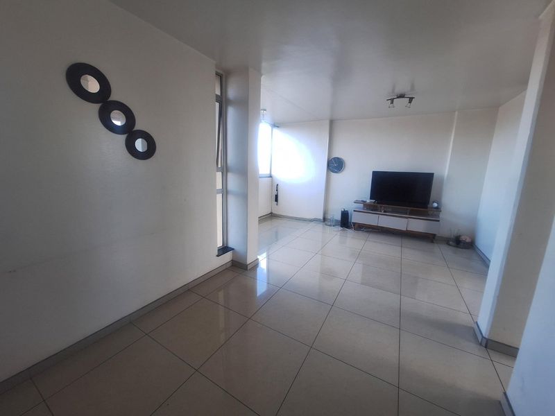 A spacious living area featuring large format floor tiles, neutral walls, and natural light from the adjacent window.