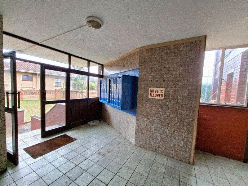 A functional apartment building entrance lobby featuring tiled flooring, built-in mailboxes, and glass panel doors providing access to the exterior.