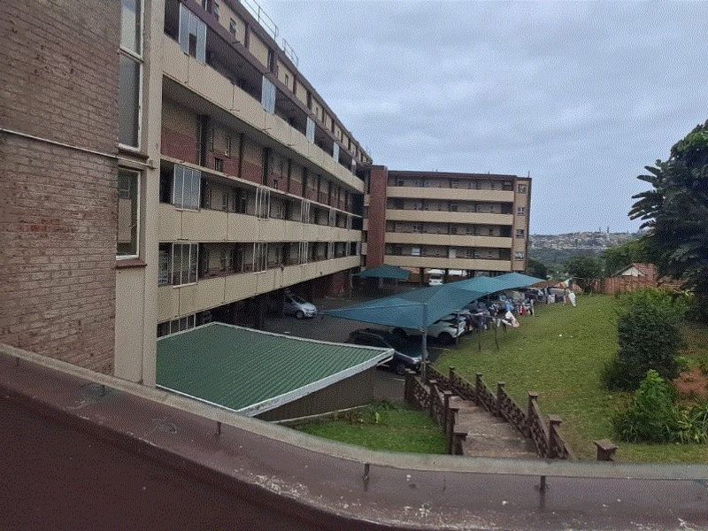 Exterior view of an apartment complex featuring multi-level balconies, a covered parking area, and a shared garden space.