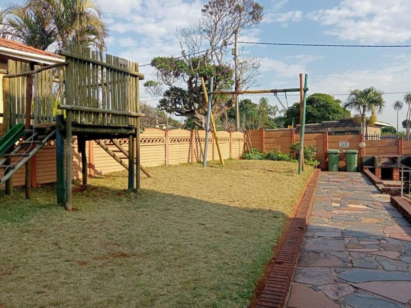 A private backyard featuring a stone-paved walkway, a built-in brick braai, and a timber play structure set within a fenced garden area.