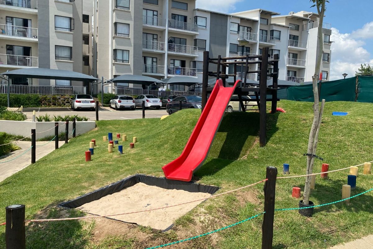 Communal outdoor area featuring a children's playground with a slide and sandpit, set against the apartment complex with dedicated parking bays.