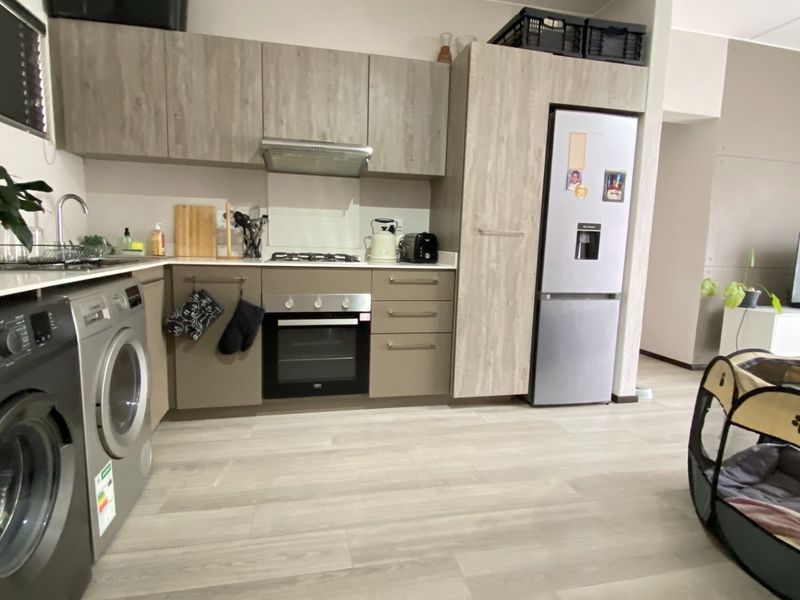 Modern open-plan kitchen featuring wood-look cabinetry, integrated appliances, and light laminate flooring, seamlessly flowing into the adjacent living area.