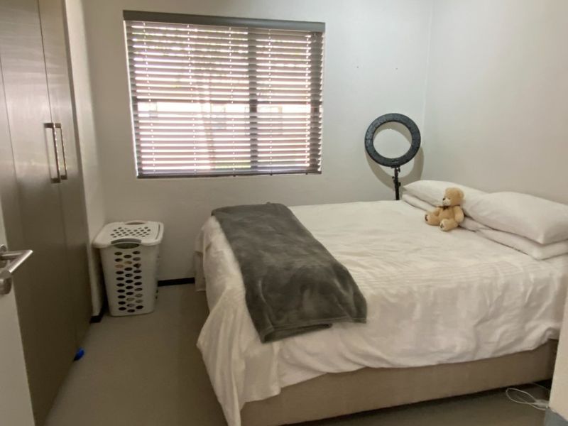 A functional bedroom featuring neutral carpeting, built-in wardrobe storage, and venetian blinds for privacy.