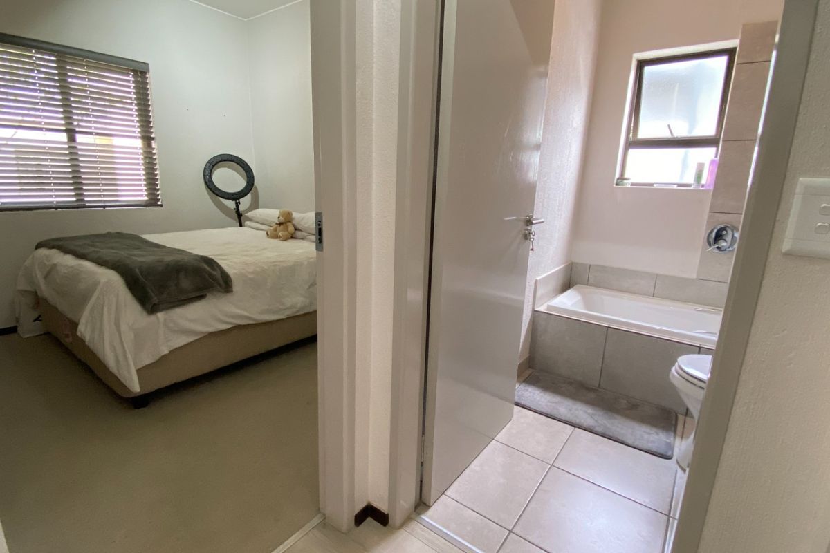 A view from a hallway looking into a bedroom with venetian blinds and an adjacent bathroom featuring a built-in bathtub and tiled flooring.