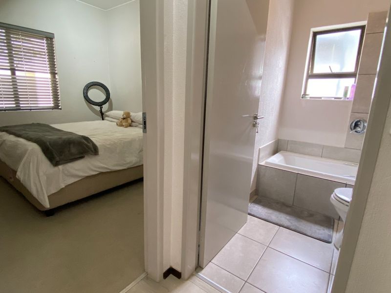 A view from a hallway looking into a bedroom with venetian blinds and an adjacent bathroom featuring a built-in bathtub and tiled flooring.