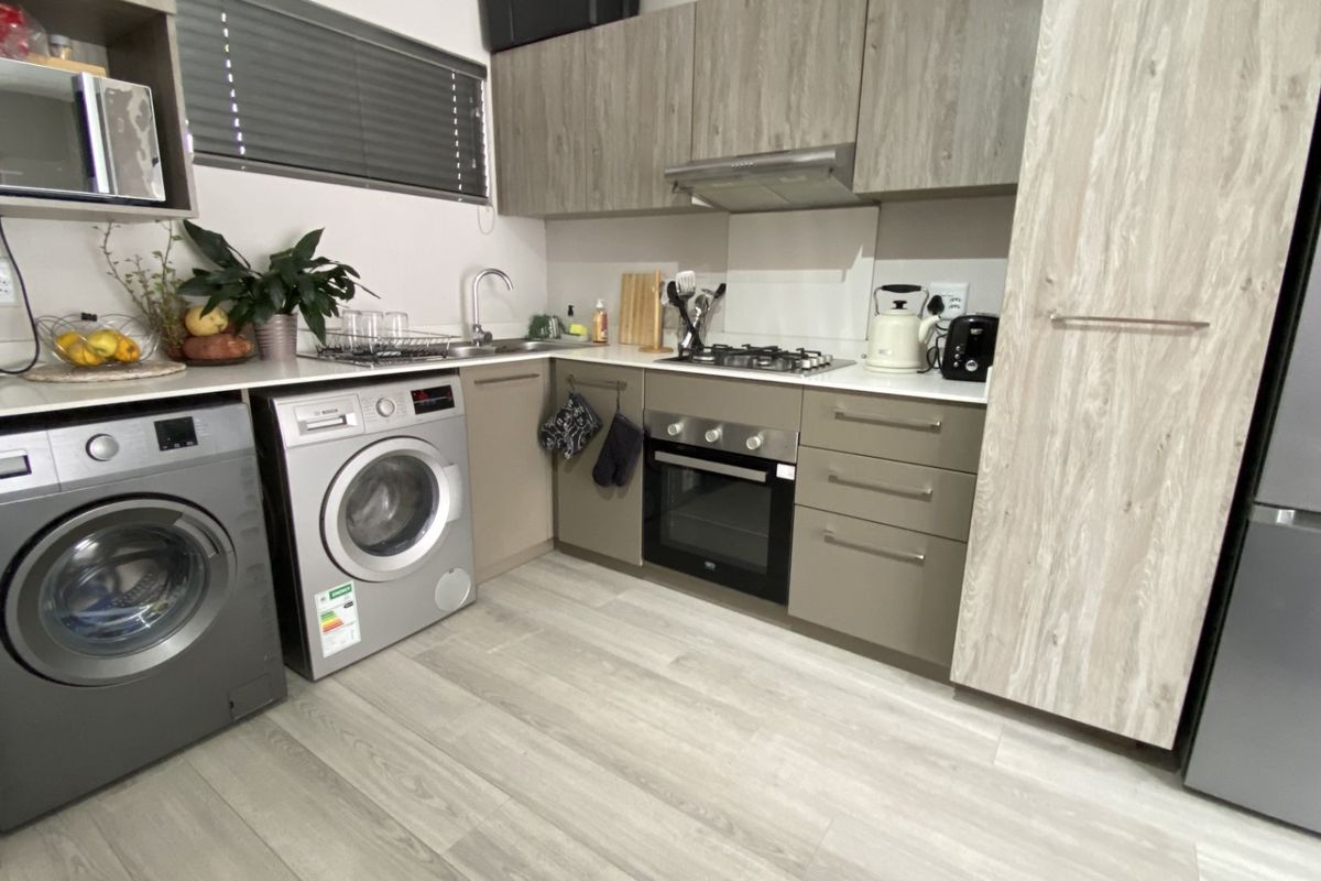 Modern kitchen featuring wood-look cabinetry, integrated oven and hob, stainless steel sink, and light laminate flooring in a compact, functional layout.