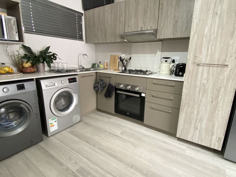 Modern kitchen featuring wood-look cabinetry, integrated oven and hob, stainless steel sink, and light laminate flooring in a compact, functional layout.