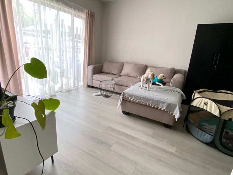 A bright living room featuring light-toned laminate flooring and a large sliding glass door that provides ample natural light.