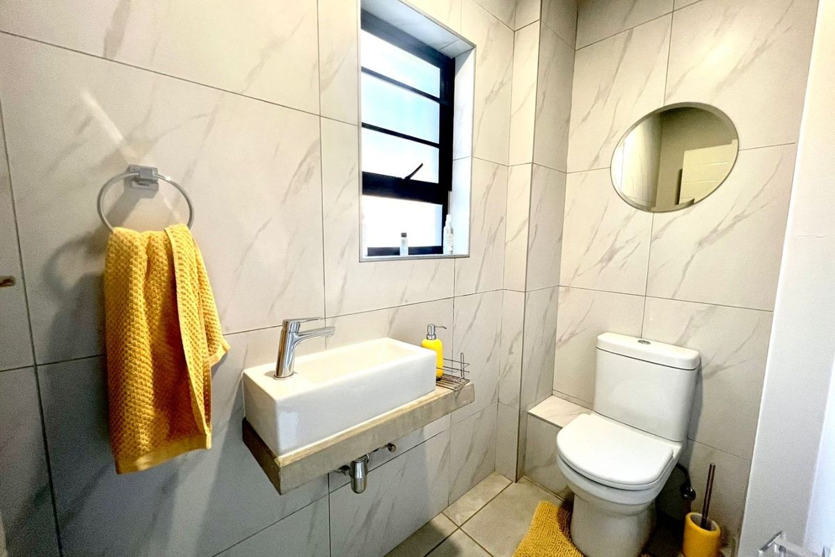 A modern, compact bathroom featuring floor-to-ceiling marble-look tiles, a wall-mounted basin, and a standard toilet.