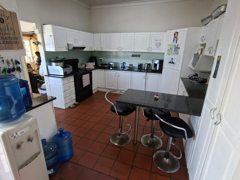 A functional kitchen featuring white cabinetry, dark granite countertops, a subway tile backsplash, and a built-in breakfast bar with tiled flooring.