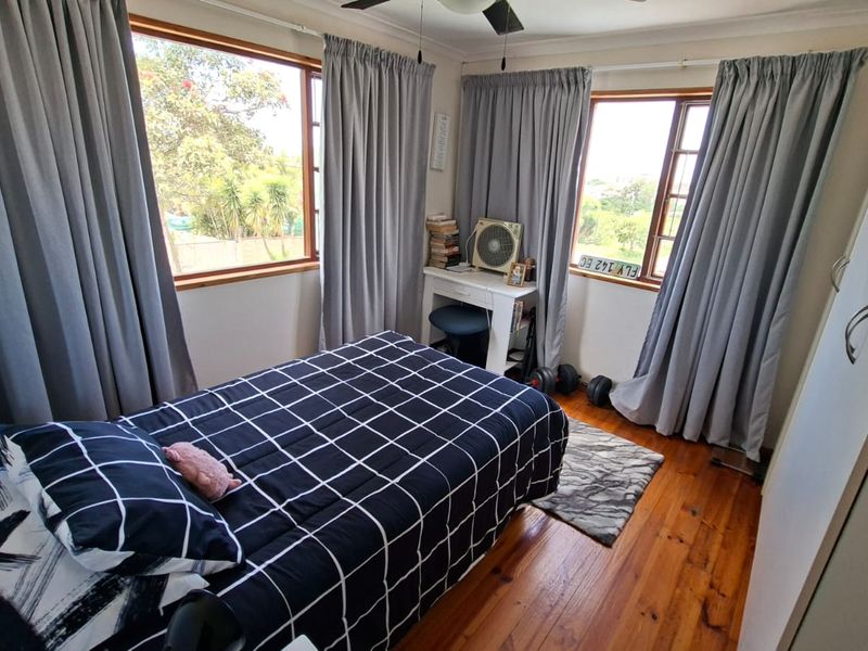 A cozy bedroom featuring warm timber flooring, a built-in wardrobe, and dual windows that provide natural light and garden views.
