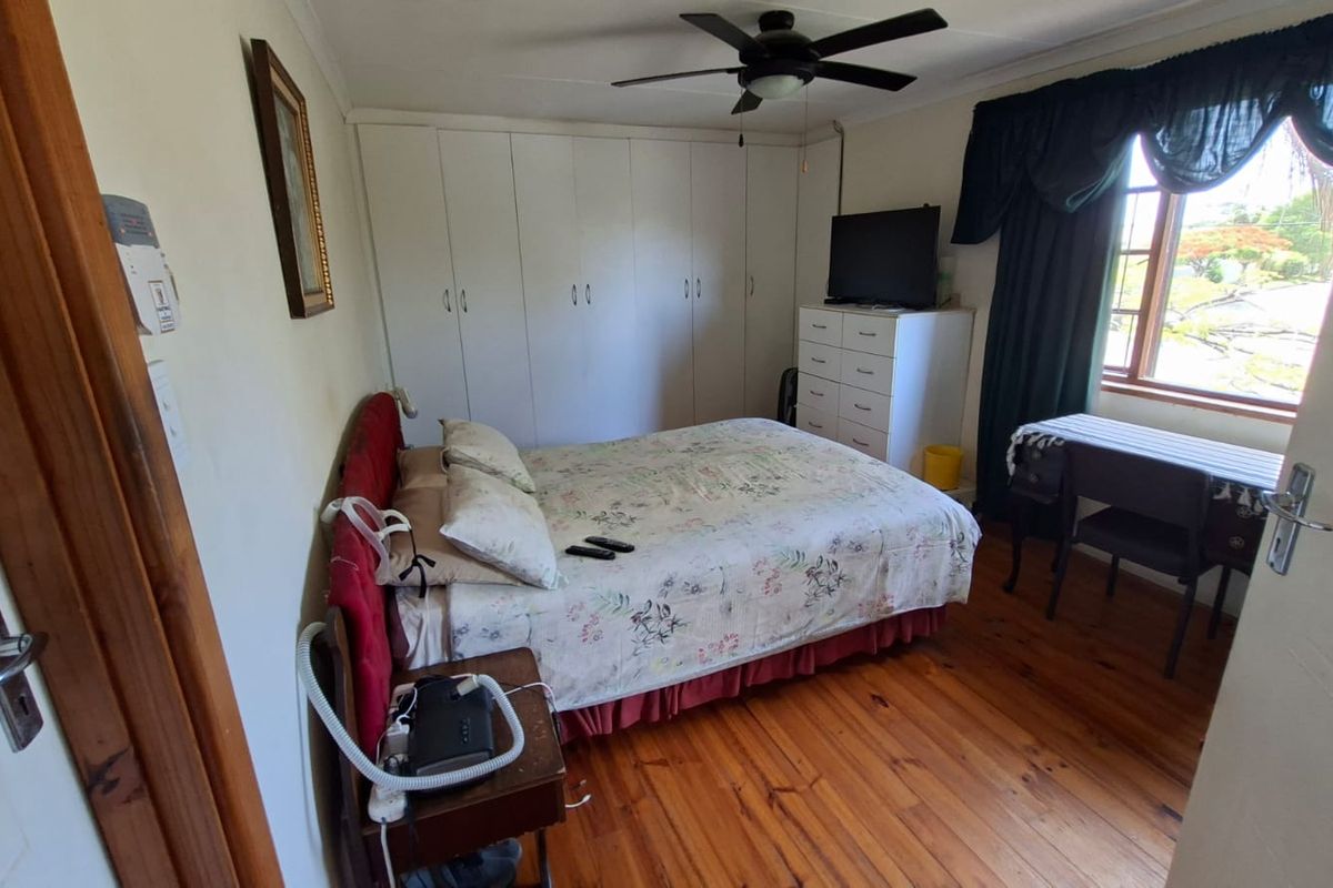 A functional bedroom featuring warm timber flooring, built-in storage cupboards, and a ceiling fan, offering a comfortable and practical living space.