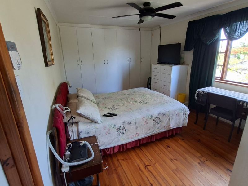 A functional bedroom featuring warm timber flooring, built-in storage cupboards, and a ceiling fan, offering a comfortable and practical living space.