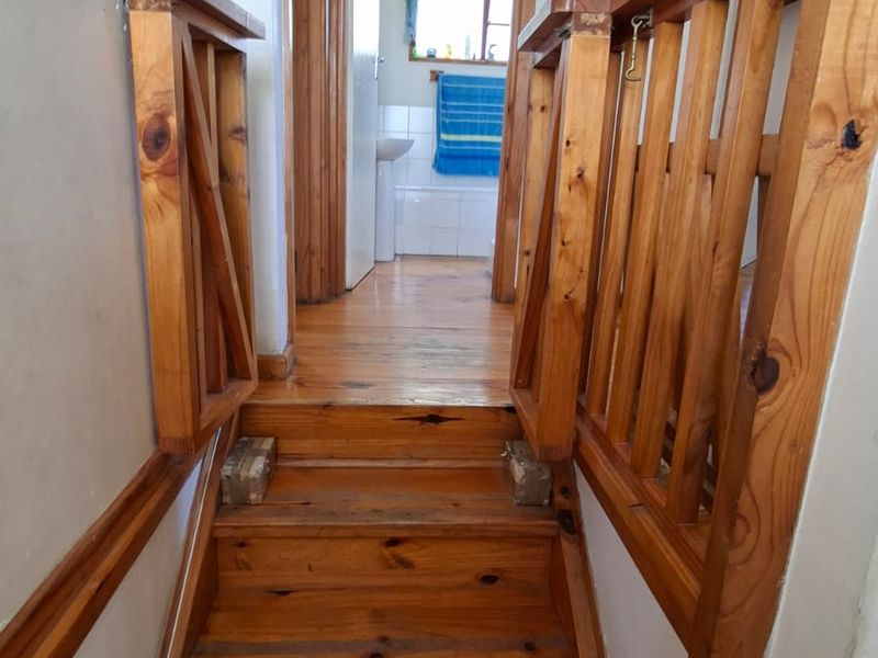 A narrow hallway featuring a timber staircase with a wooden balustrade, leading towards a bathroom area.