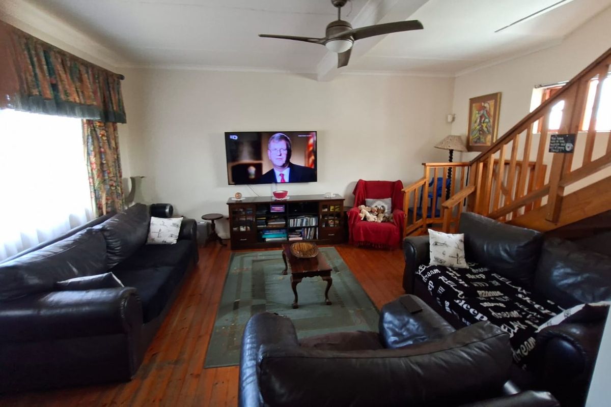 A living room featuring wooden flooring, a ceiling fan, and a wooden staircase leading to the upper level.