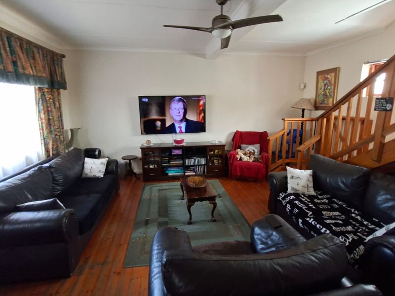 A living room featuring wooden flooring, a ceiling fan, and a wooden staircase leading to the upper level.