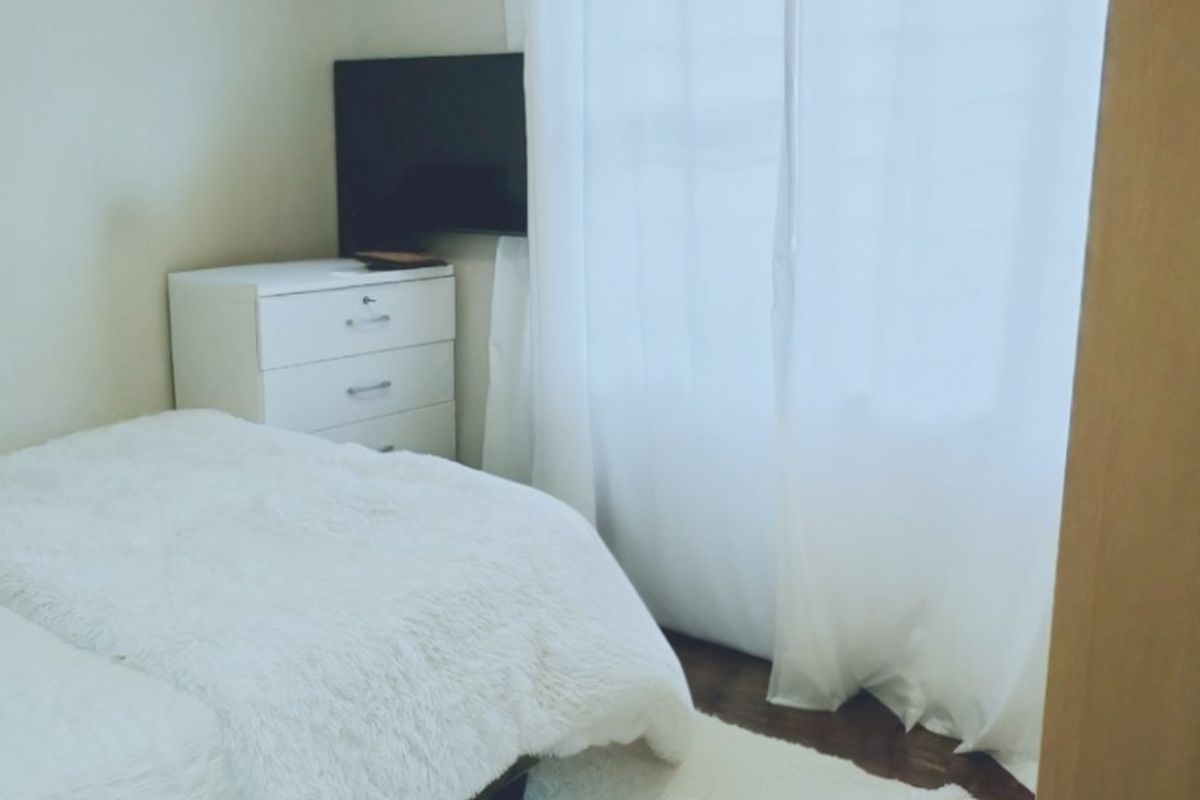 A functional bedroom featuring a wall-mounted split-system air conditioner and a window with a curtain rod.