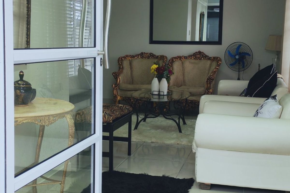 A living room area featuring tiled flooring, recessed ceiling lights, and a modern glass panel door entrance.