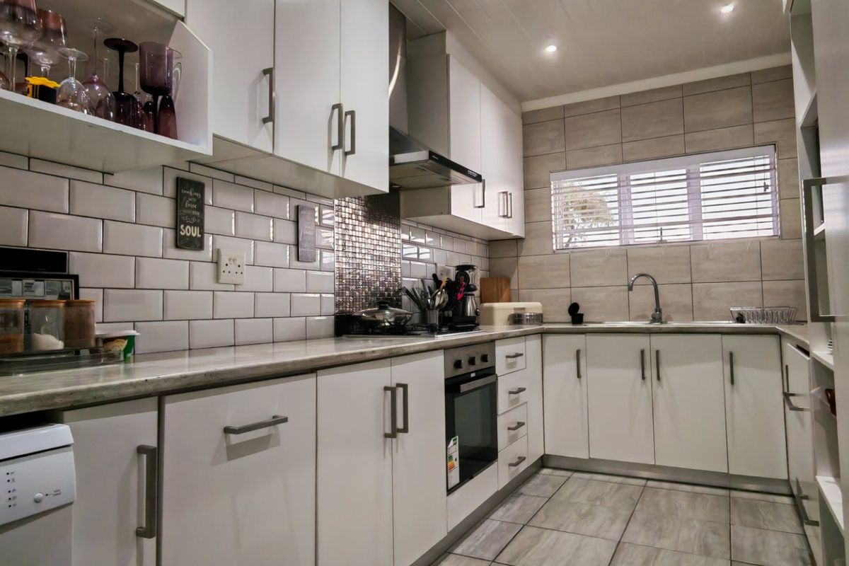 Modern kitchen featuring white cabinetry, subway tile backsplash, built-in oven, extractor fan, and stone-look countertops with tiled flooring.