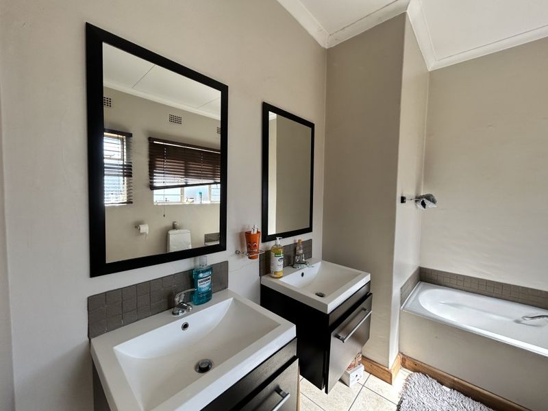A functional bathroom featuring a double vanity with modern basins, wall-mounted mirrors, and a built-in bathtub with tiled surround.