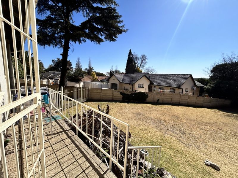 A rear view of the property featuring a concrete patio with metal railings, overlooking a spacious backyard with a precast concrete boundary wall.