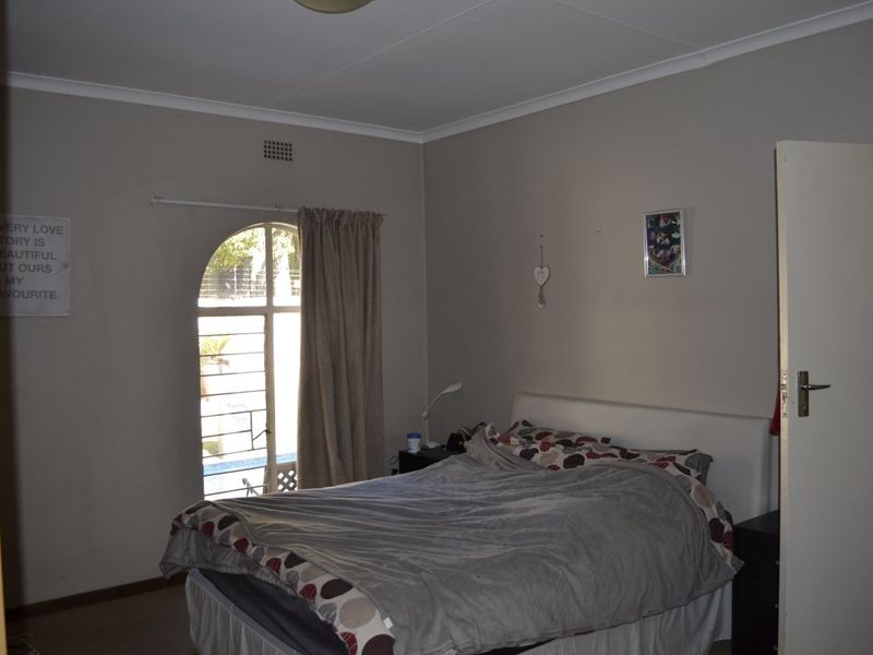 A standard bedroom featuring an arched window with security bars and neutral wall finishes.