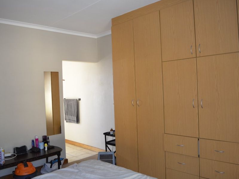 Bedroom featuring extensive light wood-finish built-in cupboards and coving, with an adjoining space visible through the doorway.