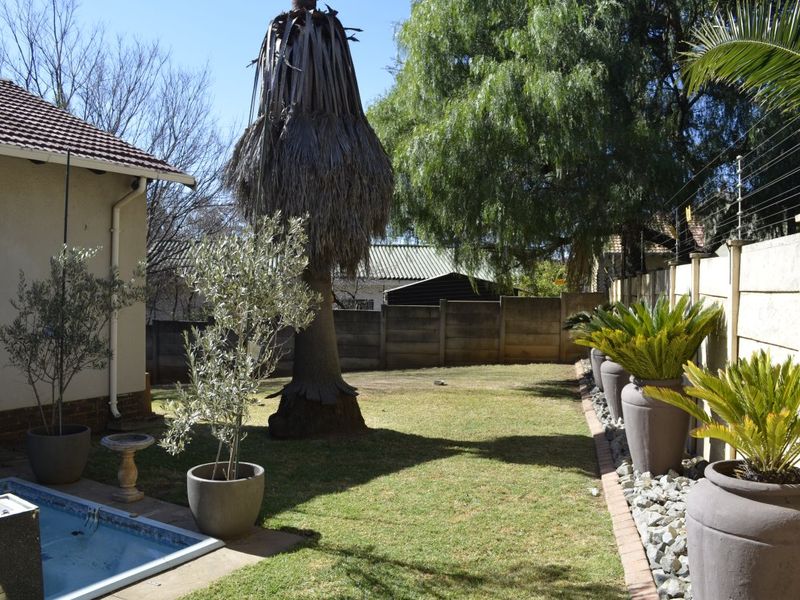 A private rear garden featuring a swimming pool, lawn area, and perimeter boundary wall with electric fencing.