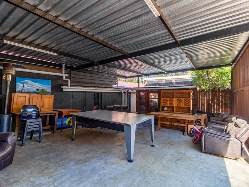 A covered outdoor patio area featuring a corrugated metal roof, exposed steel structure, and concrete flooring, suitable for outdoor entertaining.