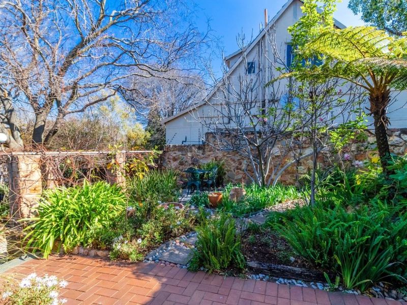 A landscaped garden featuring a brick paved patio area, stone pathways, and a rustic stone boundary wall.