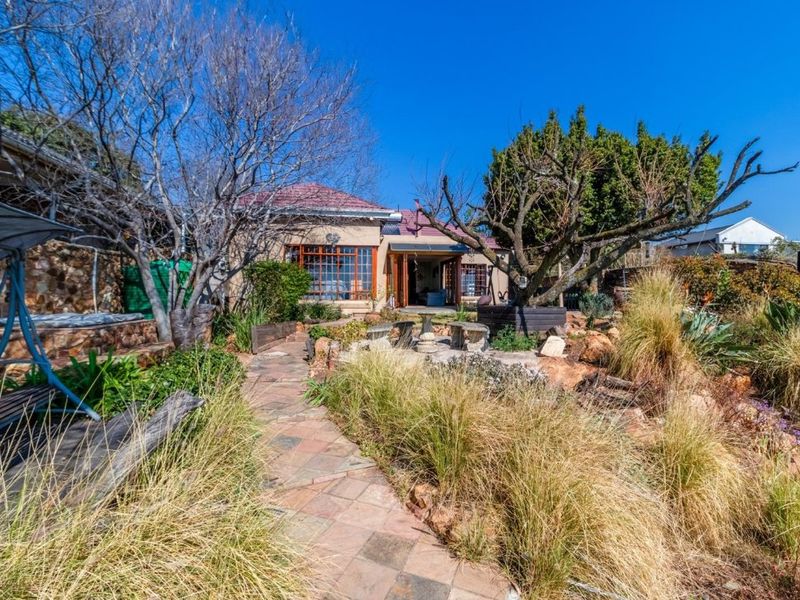 Rear view of the property featuring a stone-clad exterior, tiled roof, and a landscaped garden with a paved walkway leading to the house.