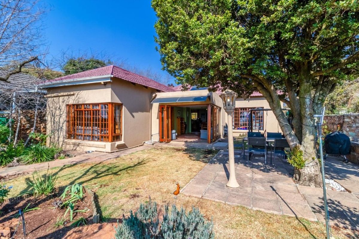 Rear view of the house featuring a paved patio area, timber-framed windows, folding glass doors, and a mature garden setting.