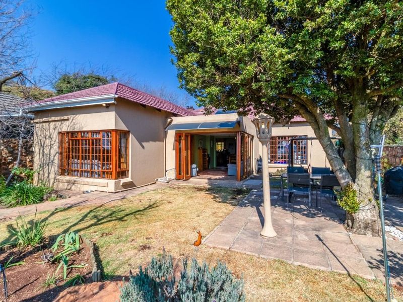 Rear view of the house featuring a paved patio area, timber-framed windows, folding glass doors, and a mature garden setting.