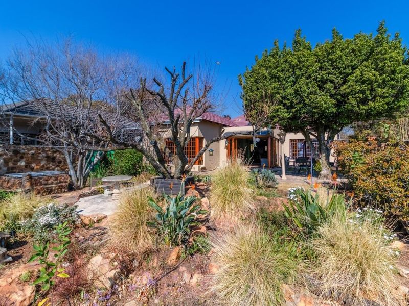 A view of the rear garden featuring a paved patio area, established landscaping, and stone retaining walls leading to the main house structure.