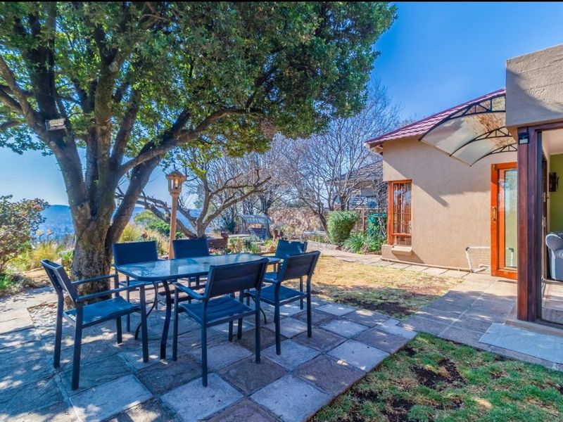 A paved outdoor patio area featuring a shaded seating space, mature tree, and direct access to the home through a sliding door.