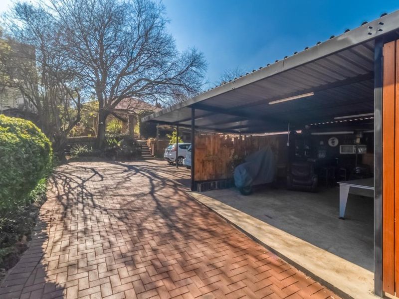 A spacious outdoor carport area with a paved driveway, featuring a metal roof structure and timber cladding accents.