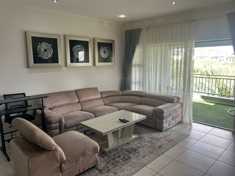 A well-lit living room featuring tiled flooring, recessed downlights, and a large sliding glass door providing direct access to an outdoor balcony area.