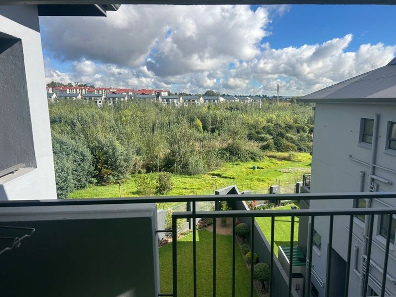 A scenic elevated view from a balcony overlooking a lush green landscape and residential neighborhood.